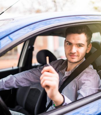 Young handsome man driving his new car, holding out keys Young man driving his new car, holding out keys